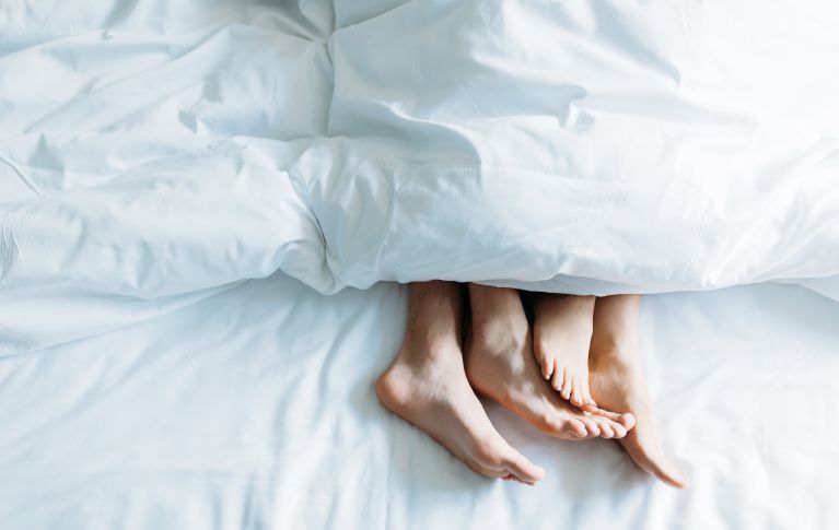 L'immagine mostra i piedi di due persone sdraiate sotto un piumone.
