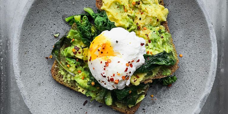 Das Bild zeigt zwei Brotscheiben mit Avocado, Spinat und Ei.