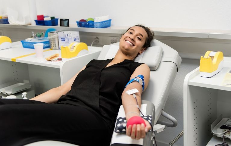 Une jeune femme souriante est allongée sur une chaise longue et donne son sang.