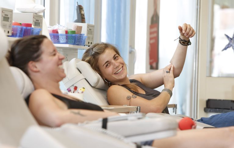 L'immagine mostra due giovani donne che ridono mentre donano il sangue.