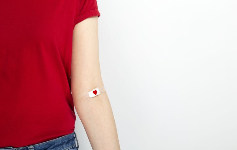 L'image montre un bras avec un bandage sur lequel est imprimé un cœur au niveau du pli du coude.