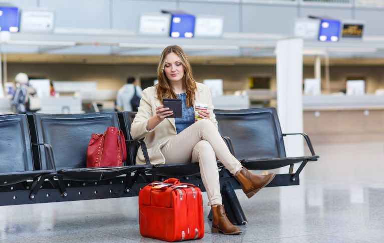 Giovane donna con una valigia rossa seduta al terminal dell'aeroporto